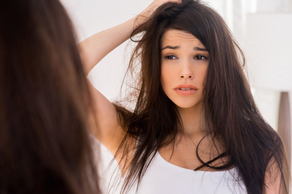 Good morning? Frustrated young woman looking at her reflection in the mirror and holding hand in hair